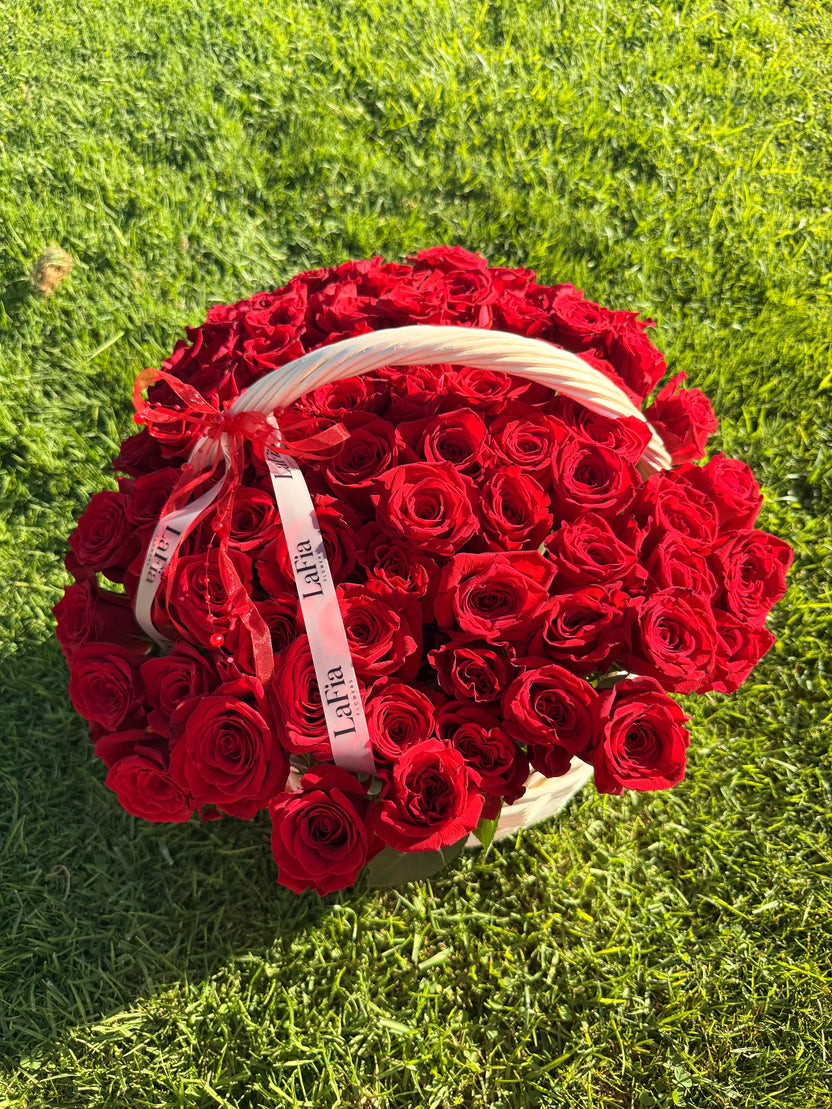 Red rose basket with white handle and LaFia ribbons photographed on grass
