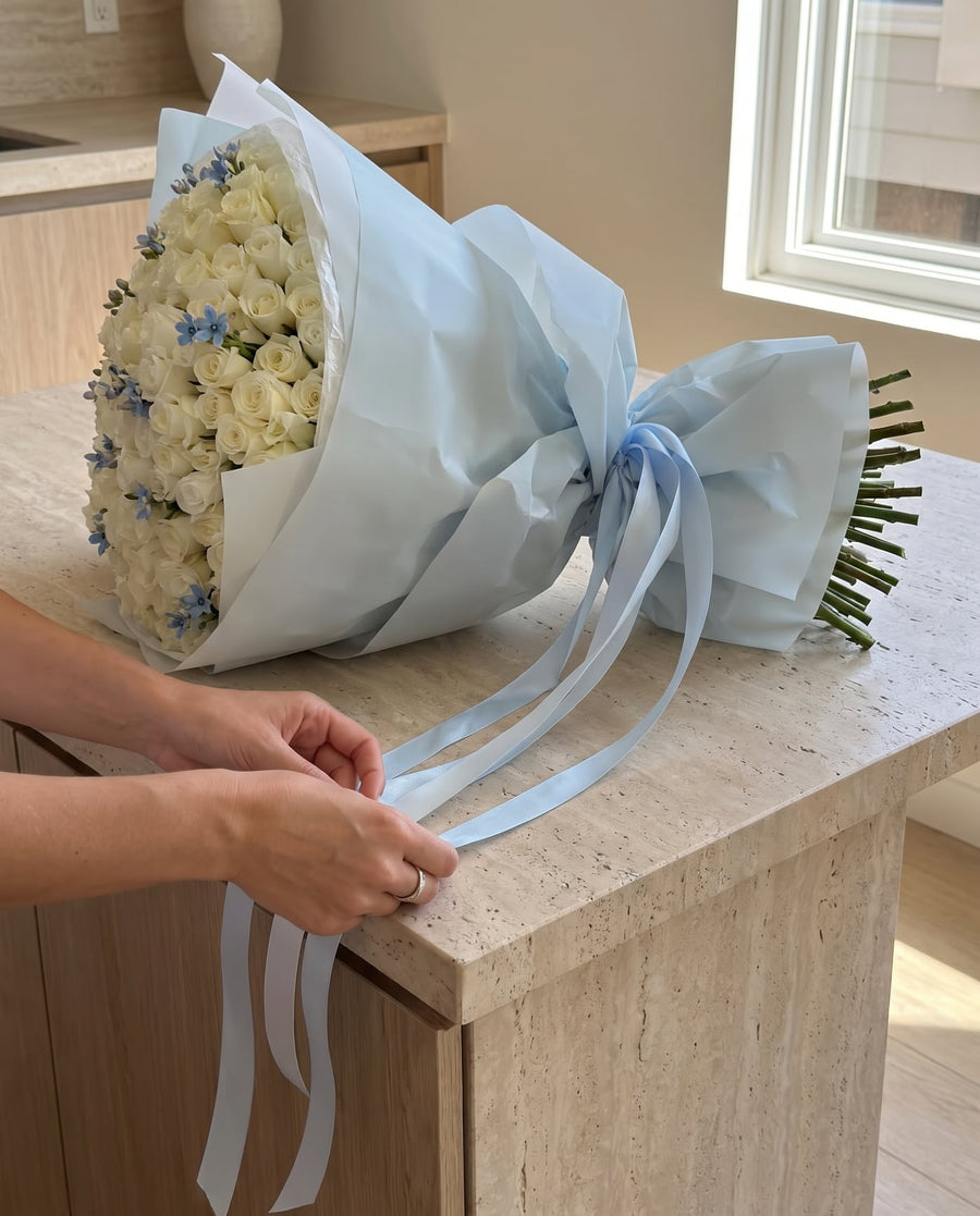 White and blue 101-rose bouquet being hand-finished with ribbon - LaFia Flowers